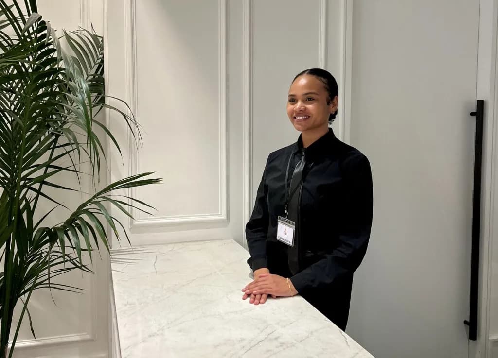 A hotel receptionist standing behind a marble reception desk